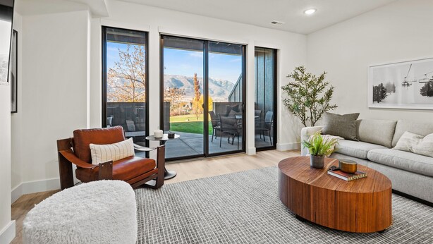 A modern living room with a leather sofa, a round coffee table, and a large sliding glass door leading to a balcony with a mountain view. - Alpine Retreat Pt A106 | Ski Escape | Mtn Views (Eden)