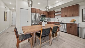 A modern kitchen with wooden cabinets, stainless steel appliances, and a dining area with a wooden table and chairs. - Alpine Retreat Pt A106 | Ski Escape | Mtn Views (Eden)