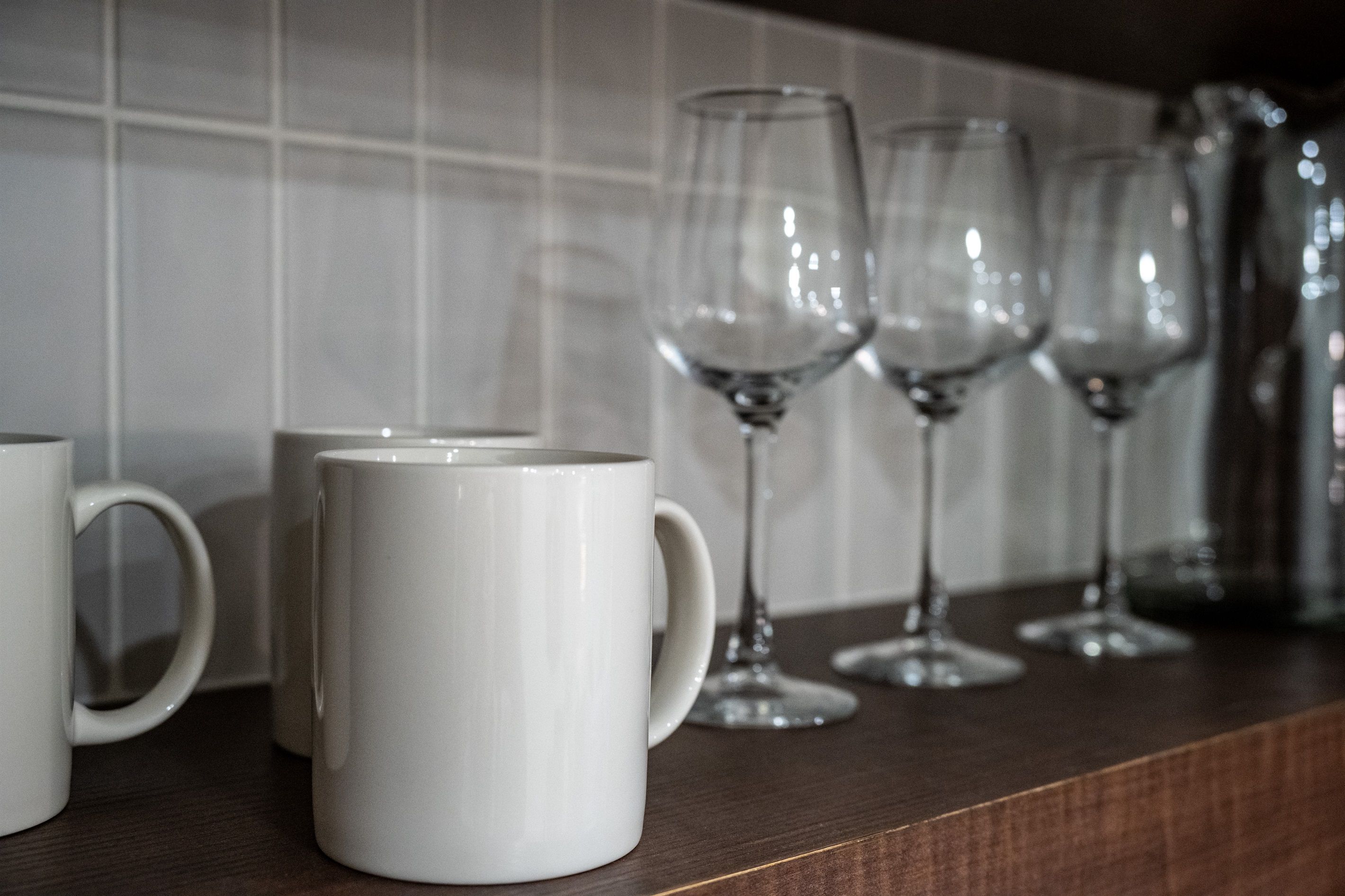 A kitchen counter with white mugs and wine glasses.