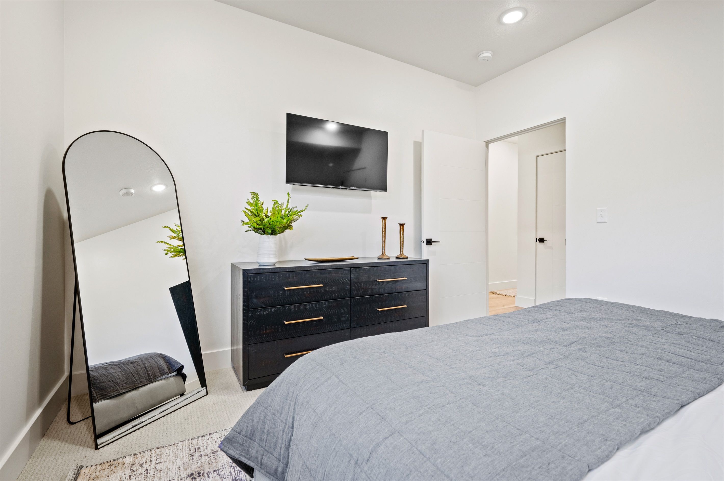 A modern bedroom with a bed, a dresser, a TV, and a mirror.