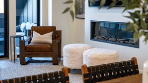 Un salon moderne avec un fauteuil en cuir marron, deux poufs blancs, un grand aquarium et une vue sur un balcon équipé d’un canapé.