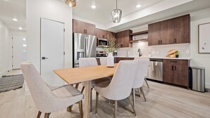 A modern kitchen with wooden cabinets, stainless steel appliances, and a dining area with a wooden table and upholstered chairs. - Powder & Golf Pt B106 | Powder Mtn Ski Retreat (Eden)