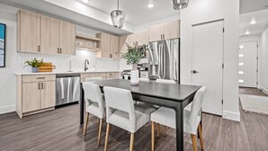 A modern kitchen with wooden cabinets, stainless steel appliances, and a dining area with a dark table and grey chairs. - Escape to Eden Pt C103|Ski Getaway |Fireplace (Eden)