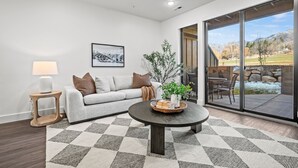 A modern living room with a sofa, coffee table, and a view of the outdoors. - Escape to Eden Pt C103|Ski Getaway |Fireplace (Eden)