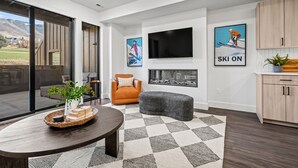 A modern living room with a large TV, a fireplace, and a view of the outdoors. - Escape to Eden Pt C103|Ski Getaway |Fireplace (Eden)