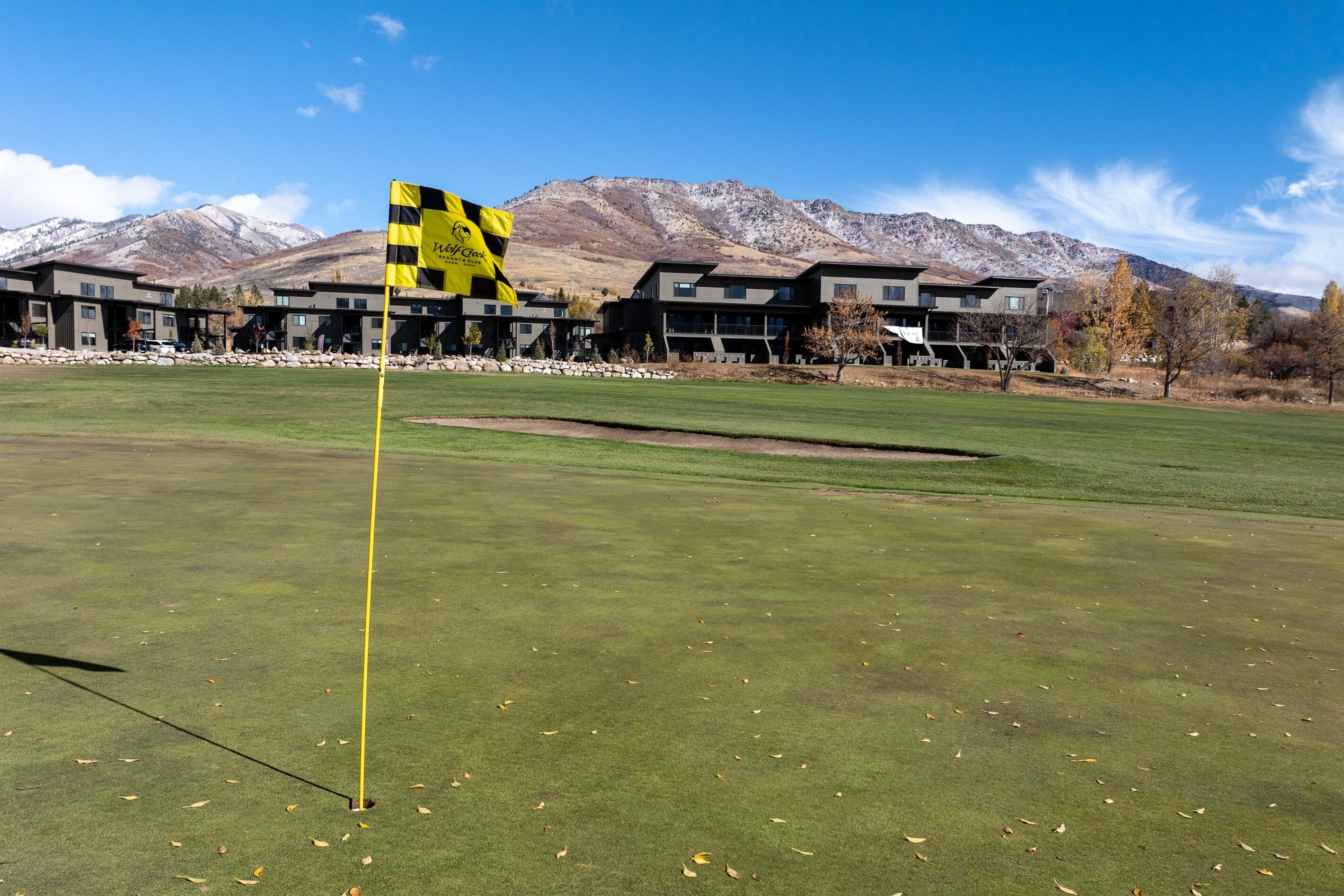 A golf course with a flagstick, a building complex in the background, and mountains.