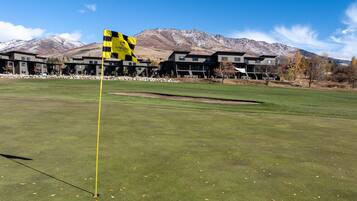 A golf course with a flagstick, a building complex in the background, and mountains.
