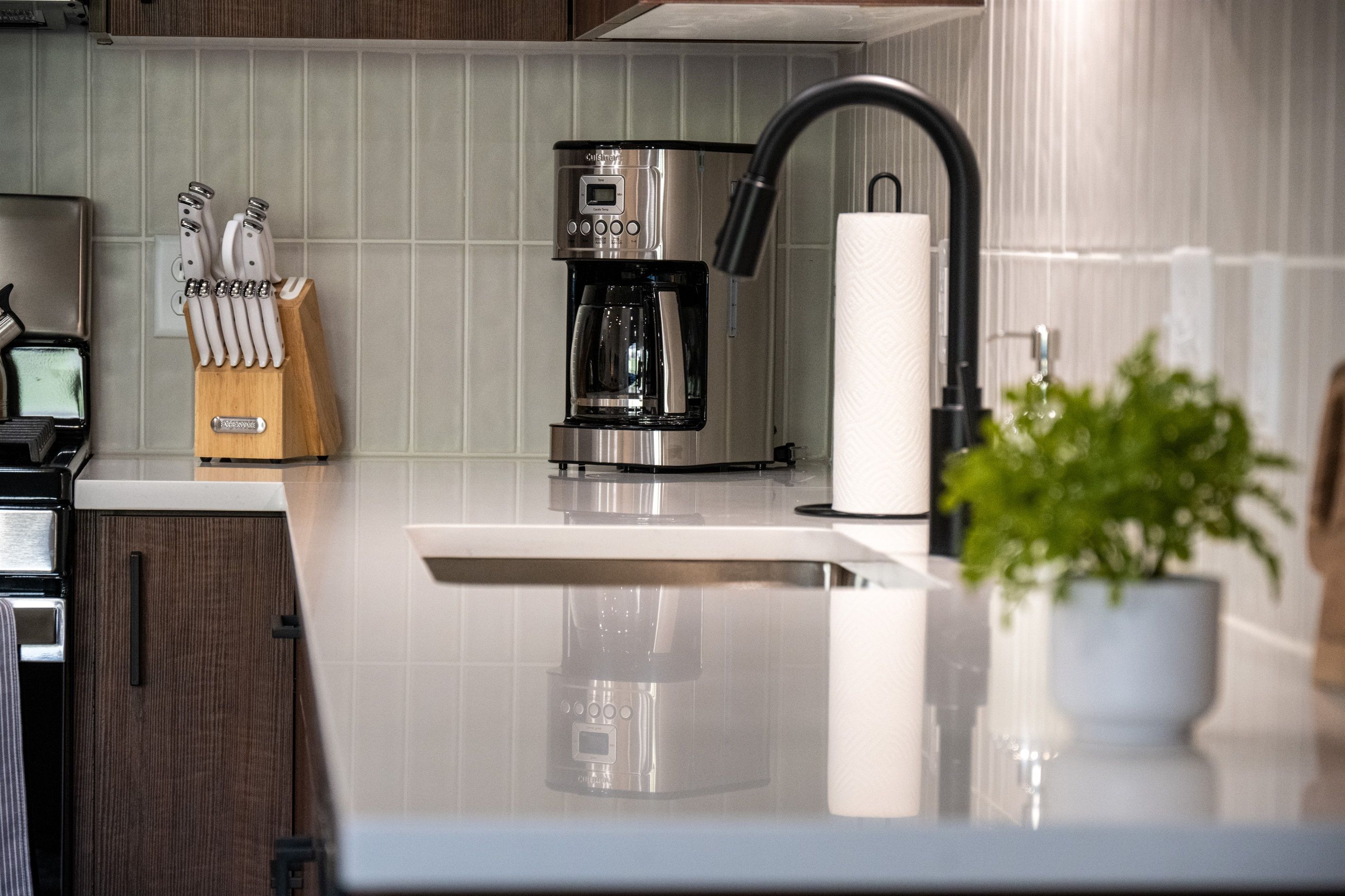 A modern kitchen with a coffee maker, knife block, and a potted plant.