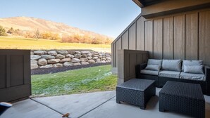 A covered patio with a stone wall, a sofa, and two ottomans. - Snowbasin Vista Retreat Pt C106 | Ski | Mtn Views (Eden)