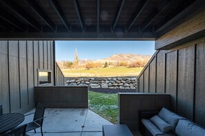 A covered outdoor seating area with a stone wall and a view of mountains. - Snowbasin Vista Pt C106 | Ski Retreat | Mtn Views (Eden)