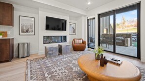 A modern living room with a fireplace, a large TV, and a view of the outdoors. - Snowbasin Vista Retreat Pt C106 | Ski | Mtn Views (Eden)