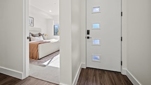Een moderne slaapkamer met een wit bed, een klein raam en een deur met een handvat.