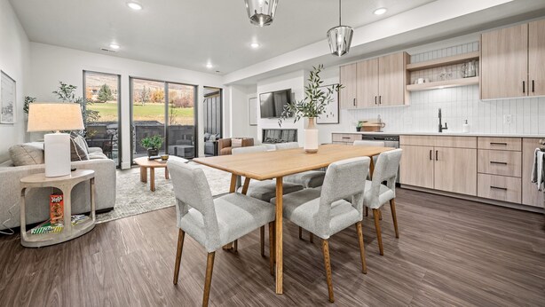 Een moderne keuken met houten kasten, een eethoek met een houten tafel en stoelen, en een groot raam met uitzicht op de omgeving.