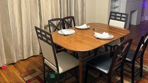 Un coin repas avec une table en bois, des chaises, un lustre et une vue sur la cuisine.