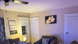 Un salon avec des canapés gris, des coussins à motifs, un ventilateur de plafond et un tapis coloré.