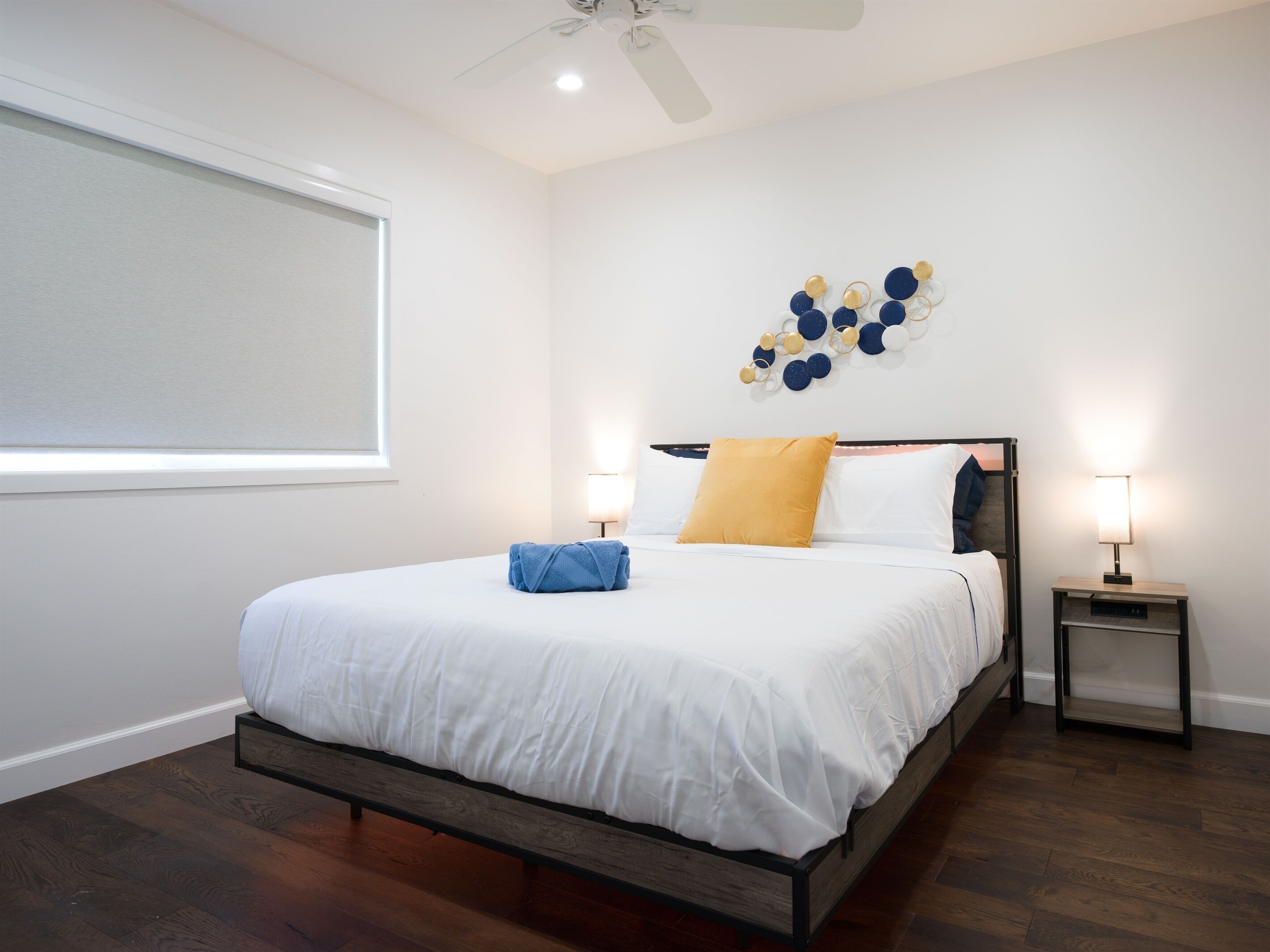 A bedroom with a bed, two bedside tables, a ceiling fan, and a wall decoration.