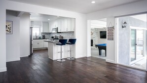 Une cuisine moderne avec des meubles blancs, un îlot central doté de tabourets et une table de billard dans la pièce adjacente.