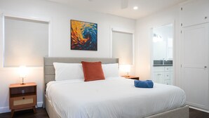 Une chambre à coucher bien rangée, avec un lit, deux tables de chevet, un ventilateur de plafond et un tableau accroché au mur.