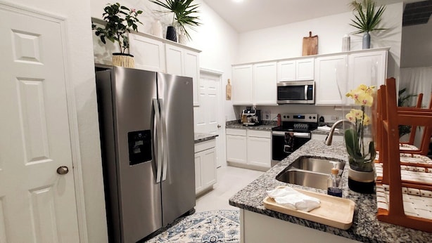 A modern kitchen with white cabinets, stainless steel appliances, a granite countertop, and a dining area with orange chairs. - Spacious 4-bedroom house in charming Port Charlotte with AC, WiFi, near beaches (Port Charlotte)