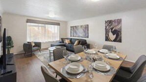 A dining area with a table set for six, a sofa, and a large window. - Barnet Oasis near Sky Studios (New Barnet)