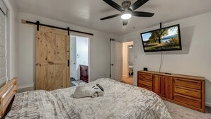 Un dormitorio con una cama, un armario de madera, un ventilador de techo y un televisor fijado a la pared.