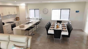 A modern kitchen with a central island, dining area with a long table, and a clock on the wall. - TWIN GUMS - EXCLUSIVE RIVERFRONT PROPERTY - TAILEM BEND (Tailem Bend)