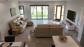 A modern living room with a sofa, a coffee table, and a TV. There is a sliding glass door leading to a balcony. - TWIN GUMS - EXCLUSIVE RIVERFRONT PROPERTY - TAILEM BEND (Tailem Bend)