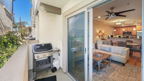 A balcony with a barbecue grill, sliding glass doors leading to a living room with a sofa, coffee table, and kitchen area with cabinets and appliances. - Just Beachy: a charming townhome steps from Beach & Boardwalk in Pacific Beach! (San Diego)