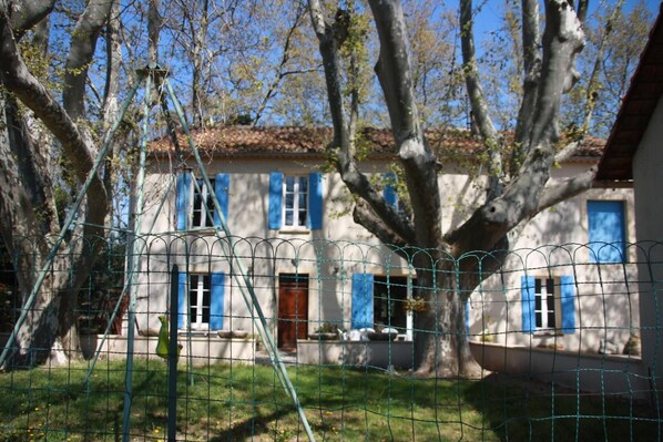 Una casa con contraventanas azules, un árbol en primer plano y un cielo despejado.
