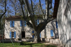 A two-story house with blue shutters, a large tree in front, and a clear sky.