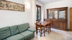 A dining area with a wooden table and chairs, a green sofa, and a cabinet with glass doors. - 'Alassio Holiday' Apartment with Private Garden (Alassio)