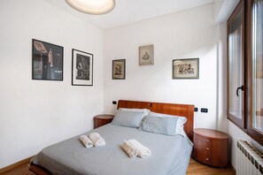Een keurig opgemaakt bed met kussens, een nachtkastje en een wand met ingelijste foto's.