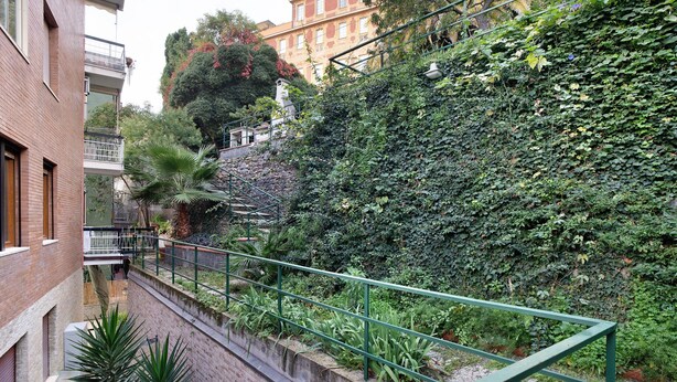 A narrow urban pathway with a green metal railing, brick buildings, and dense greenery. - 'Alassio Holiday' Apartment with Private Garden (Alassio)