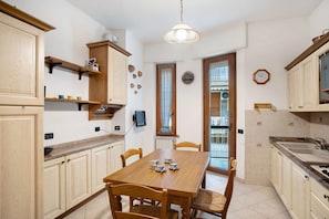 Una cocina con armarios de madera, una mesa de comedor con sillas, una lámpara colgante y una ventana con cortinas.