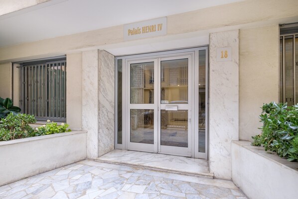 A building entrance with a sign reading 'Palais Henri IV,' a glass door, and a number '18' on the wall.