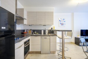 A compact kitchen with a dishwasher, oven, and a small dining area with a chair.