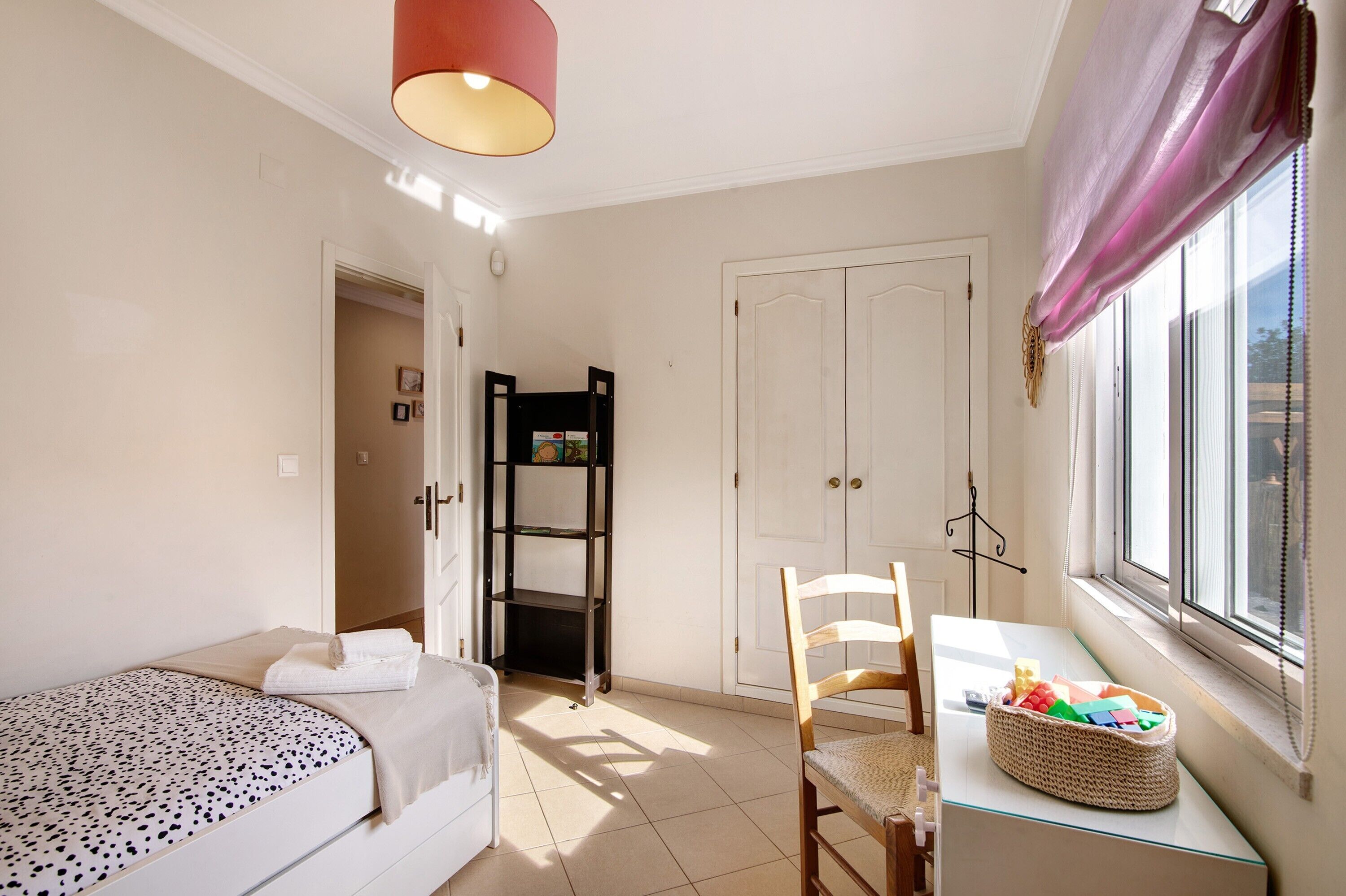 A bedroom with a bed, a desk, a chair, a window with curtains, and a wardrobe.