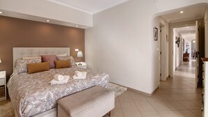 A bedroom with a large bed, bedside tables, a bench, and a hallway leading to other rooms.
