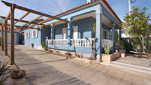A blue house with a covered porch, potted plants, and outdoor furniture.