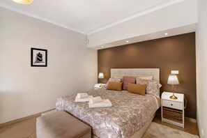 A bedroom with a large bed, bedside tables, a nightstand, a framed picture on the wall, and a window. - Holiday Home 'Casa Das Buganvilias' with Mountain View, Private Terrace and Wi-Fi (Loulé)