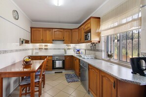 Una cocina con armarios de madera, microondas, pileta y una mesa de comedor con sillas.