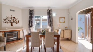 A dining room with a fireplace, a dining table with chairs, a cabinet, and a view through the window.