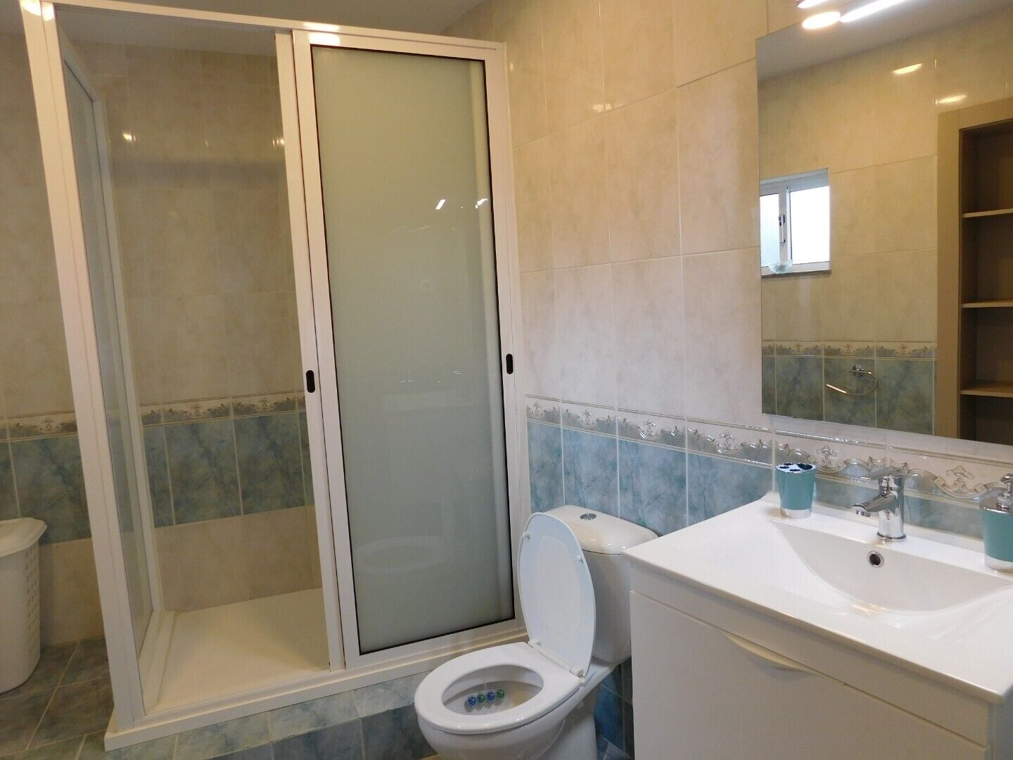 Een badkamer met een douche met glazen wand, een toilet en een wastafel met spiegel erboven.