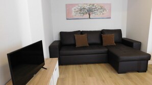 A modern living room with a black sectional sofa, a flat-screen TV, and a painting of a tree on the wall. - Holiday Home 'Casa Da Veiga - Natureza E Cidade' with Private Terrace, Wi-Fi and Air Conditioning (Lago)