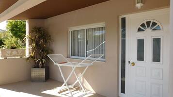 Una puerta blanca con un panel de vidrio, una silla metálica blanca, una planta en maceta y una ventana con persianas.