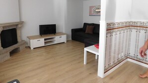 A living room with a fireplace, a television on a wooden stand, a black sofa, and a white coffee table. - Holiday Home 'Casa Da Veiga - Natureza E Cidade' with Private Terrace, Wi-Fi and Air Conditioning (Lago)