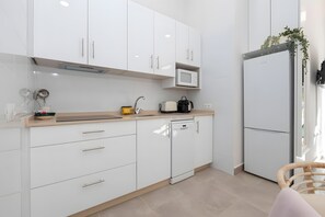 Cocina moderna con gabinetes blancos, microondas, lavavajillas y ventana con planta.