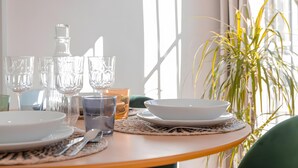 A dining table with clear glassware, plates, and a candle, set against a window with natural light and a potted plant.