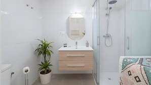 A modern bathroom with a white vanity, a large mirror, a shower, and a potted plant.