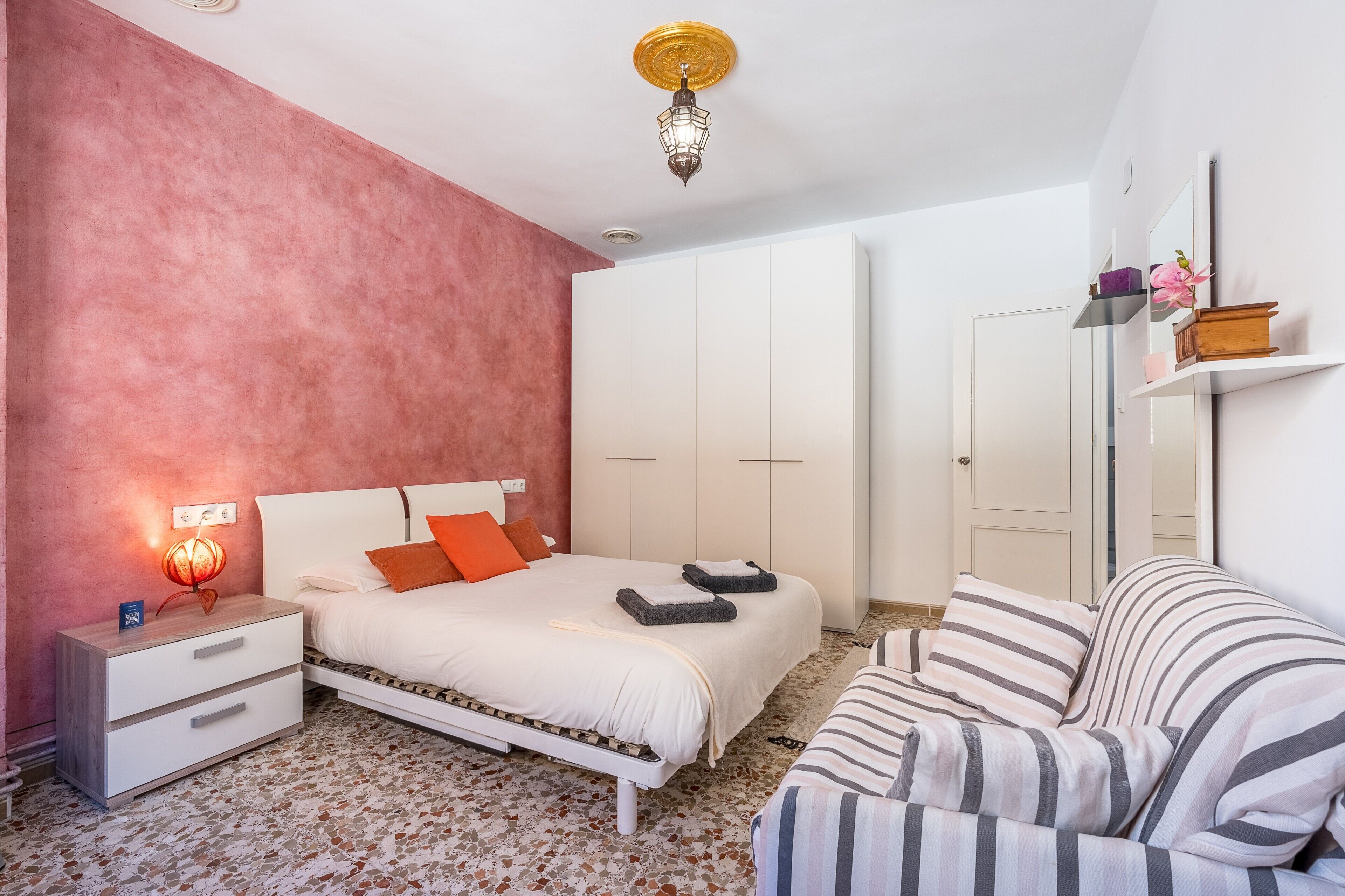 A bedroom with a bed, bedside table, nightstand, and a mirror on the wall.